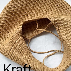 May include: A tan, round, woven hobo bag with a textured surface and thin, matching woven straps. The bag features a wide, open top and a consistent, dense braided pattern throughout its construction. The word Kraft is printed in black text.