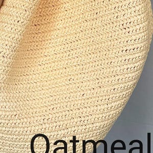May include: A close-up view of a light beige, woven straw bag with a textured, braided surface. The word Oatmeal is printed in a bold, black, sans-serif font across the lower portion of the bag, clearly visible against the light-colored material.