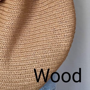 May include: A large, tan, woven straw tote bag with a textured, braided surface. The word Wood is printed in black, sans-serif capital letters in the lower right corner of the bag. The bag is positioned against a plain, light-colored background.
