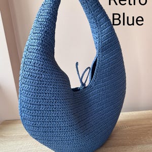 May include: A crescent-shaped hobo bag crafted from blue woven material with a single integrated shoulder strap and a small tie closure at the top opening. The text Retro Blue is printed in black on the upper right side of the image.