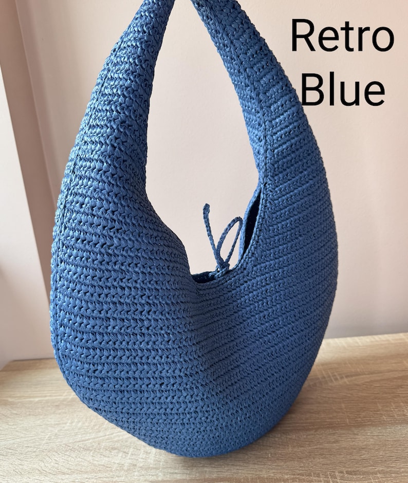 May include: A crescent-shaped hobo bag crafted from blue woven material with a single integrated shoulder strap and a small tie closure at the top opening. The text Retro Blue is printed in black on the upper right side of the image.