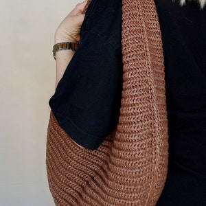 May include: A brown hobo-style shoulder bag crafted from a woven, textured material. The bag features a wide, integrated shoulder strap and a curved, slouchy silhouette with a consistent braided pattern throughout the entire exterior surface.