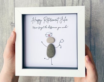 May include: White framed picture with a hand-drawn illustration of a nurse made from stones. The text reads "Happy Retirement Julie. Never forget the difference you made!"