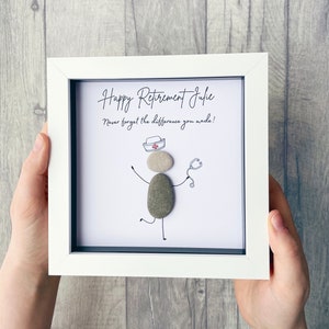 May include: White framed picture with a hand-drawn illustration of a nurse made from stones. The text reads "Happy Retirement Julie. Never forget the difference you made!"