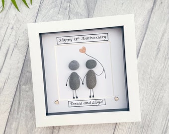May include: A white frame with a white mat and a white background. The background has a drawing of two people made of gray stones holding hands. The drawing has a small pink heart with a string attached to it. The text "Happy 35th Anniversary" is at the top of the frame. The text "Teresa and Lloyd" is at the bottom of the frame.