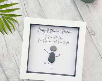 Op de afbeelding: Witte ingelijste afbeelding met een handgetekend figuur van grijze stenen die een glas wijn vasthouden. De tekst luidt "Happy Retirement Marie To New Adventures New Memories & A New Chapter".
