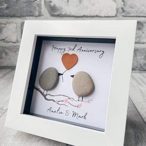 May include: A white framed picture with a hand-painted design of two birds holding a heart-shaped balloon. The text "Happy 3rd Anniversary Amelia & Mark" is written below the birds.