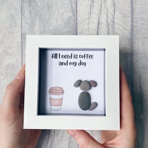 May include: White framed picture with a grey background. The picture says "All I need is coffee and my dog." There is a drawing of a coffee cup and a dog made out of pebbles.