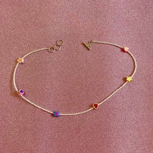 Op de afbeelding: Een witte kralenketting met kleurrijke hart- en sterbedels. De ketting heeft een zilveren sluiting en is perfect om elke outfit een vleugje speelsheid te geven.