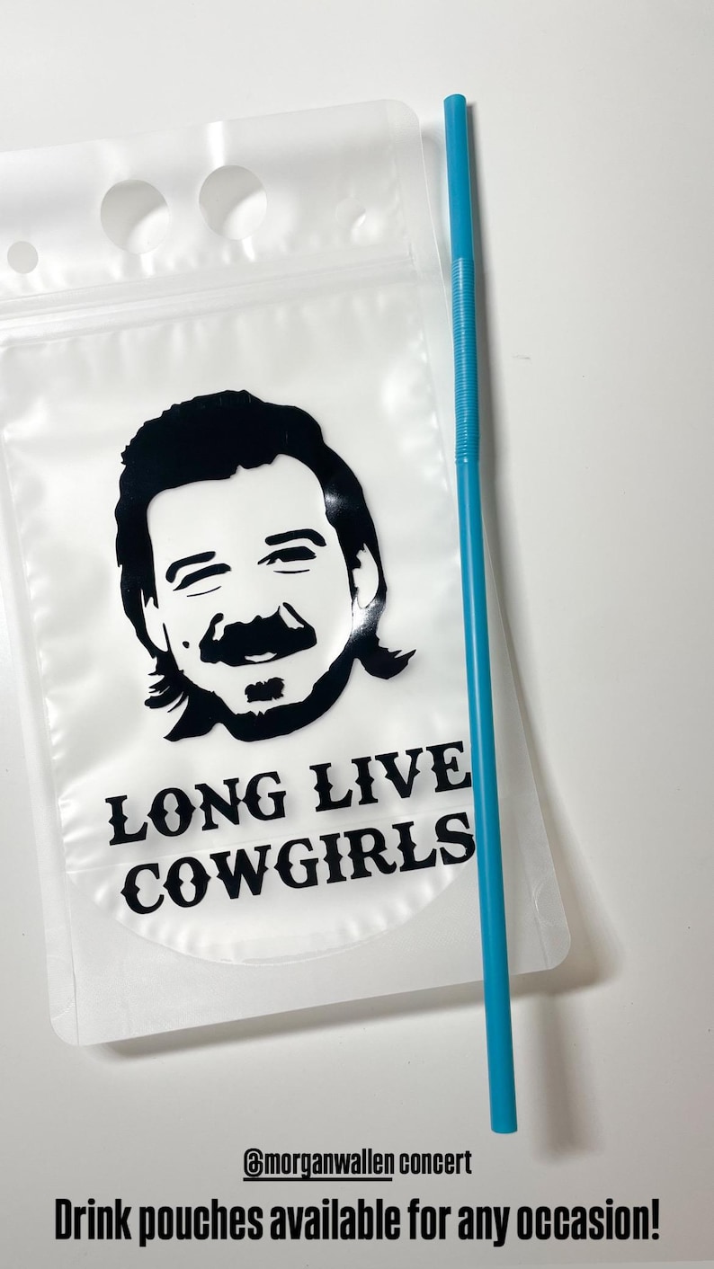 Op de afbeelding: Een doorzichtige plastic drinkzak met een zwarte grafische illustratie van een persoon met een snor en een matje, met de tekst LONG LIVE COWGIRLS eronder gedrukt. Een lang, dun, felblauw plastic rietje ligt naast de drinkzak.