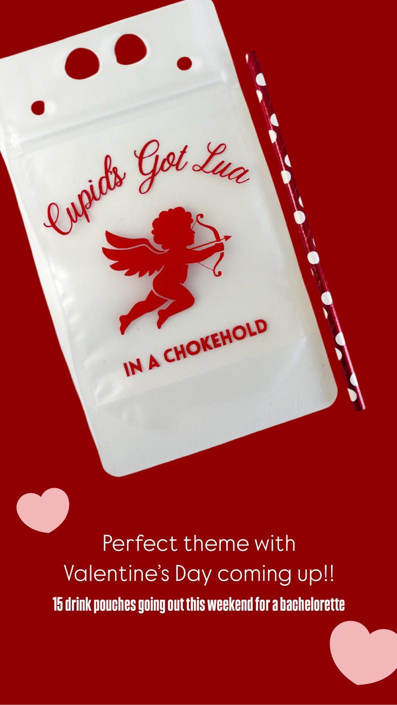 Op de afbeelding: Een doorschijnend drinkzakje met een rode afbeelding van een cherubijn met pijl en boog. De tekst luidt "Cupid's Got Lua" in cursief en "IN A CHOKEHOLD" in blokletters. Een rood-wit gestippeld rietje ligt naast het drinkzakje.