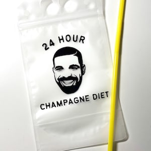 Op de afbeelding: Een doorzichtig, flexibel plastic drinkzakje met een hersluitbare bovenkant en twee ronde uitsparingen om te dragen. Het zakje is voorzien van een zwarte afbeelding van een lachend gezicht van een man met de tekst 24 HOUR CHAMPAGNE DIET in het zwart, vergezeld van een geel rietje.