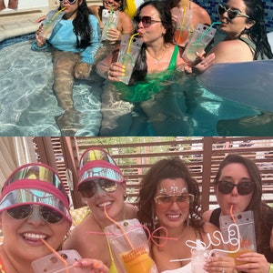 Op de afbeelding: Doorzichtige plastic drinkzakjes met rietjes, voorzien van de tekst "SCOTTSDALE BACHELORETTE". De flexibele, rechthoekige zakjes bevatten een oranje vloeistof en zijn ontworpen voor het onderweg drinken van dranken tijdens sociale buitenactiviteiten.