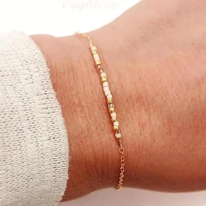 May include: A delicate gold chain anklet featuring a central row of small, alternating cream-colored and metallic gold beads. At the bottom of the image, a white rectangular graphic displays the brown text Auntie, a heart symbol, and Est. 2025.