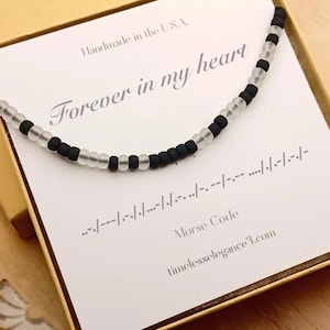 May include: A beaded necklace featuring alternating matte black and translucent white beads arranged in a Morse code pattern. The necklace is displayed on a white card printed with the text Forever in my heart, Handmade in the U.S.A., Morse Code, and the website address timelesselegance3.com.