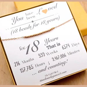 May include: A gold-filled necklace with 18 beads, presented on a card that reads "You have been Loved" and "18 beads for 18 years." The card also lists the equivalent time in months, weeks, days, hours, and minutes.