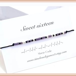 May include: A black string bracelet with purple and silver beads. The bracelet spells out "sweet sixteen" in Morse code. The card reads "Sweet sixteen .../---/././-.../../-..-/-/-/-/-- Morse Code www.timelesselegances.etsy.com"