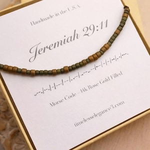 May include: A beaded necklace with a Morse code design, presented in a gift box. The necklace features a mix of brown and olive-green beads. The card inside the box reads "Jeremiah 29:11" and "Morse Code - 14k Rose Gold Filled."