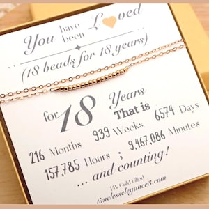 May include: A gold-filled necklace with 18 beads, presented on a card. The card reads "You have been loved" and "for 18 years", with calculations of days, weeks, months, hours, and minutes. The website address is timelesselegances8.com.