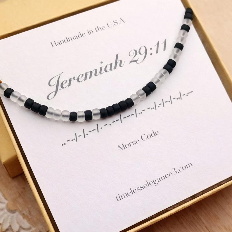 May include: A beaded necklace with alternating black and clear beads, presented in a gift box. The necklace is displayed on a card with the text "Jeremiah 29:11" and Morse code. The box also includes the text "Handmade in the U.S.A."