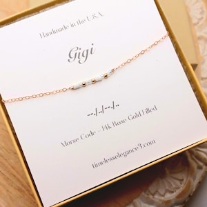 May include: A rose gold filled Morse code bracelet with white and gold beads, presented in a gift box. The card reads "Gigi" and "Handmade in the U.S.A." with the website timelesselegance3.com.