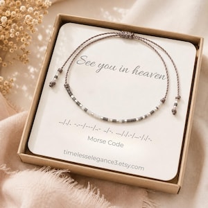 May include: A delicate cord bracelet featuring small grey and white beads arranged in a Morse code pattern. The bracelet is displayed on a white card inside a box, with the text See you in heaven and Morse Code printed on the card.