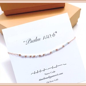 May include: White and rose gold beaded bracelet with the text "Psalm 150:6" and the morse code translation. The bracelet is on a white card with the text "timelesselegances.com" and "14k Rose Gold".