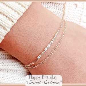 May include: A silver bracelet with a delicate chain and a row of small white beads. The bracelet is worn on a person's wrist. The text "Happy Birthday "Sweet Sixteen"" is written below the image.