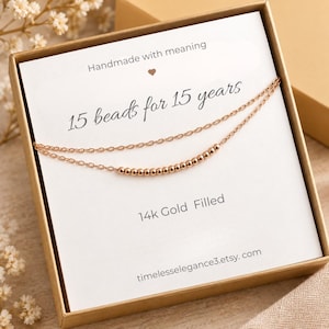 May include: A double-strand 14k gold filled necklace featuring 15 small beads on one chain, presented in a box with a card that reads: Handmade with meaning, 15 beads for 15 years, 14k Gold Filled, and the website address timelesselegance3.etsy.com.