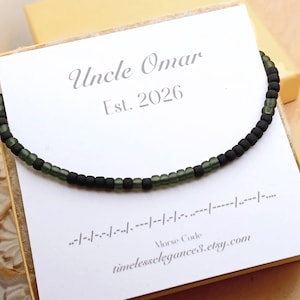 May include: A beaded necklace with alternating black and green beads, resting on a white card. The card reads "Uncle Omar Est. 2026" and features Morse code. The Etsy shop URL is also visible.