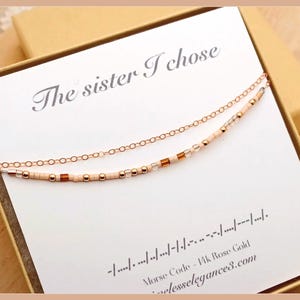 May include: A rose gold necklace with two strands, one a delicate chain and the other adorned with small beads and accents. The necklace is presented on a card that reads "The sister I chose" and includes Morse code.