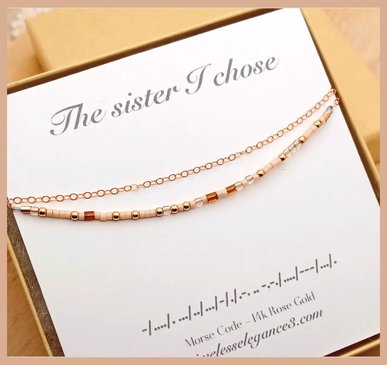 May include: A rose gold necklace with two strands, one a delicate chain and the other adorned with small beads and accents. The necklace is presented on a card that reads "The sister I chose" and includes Morse code.