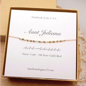 May include: Aunt Juliana Morse code bracelet in a gift box. The bracelet is rose gold filled with a delicate chain and beads. The card reads "Handmade in the U.S.A." and "timelesselegance3.com".