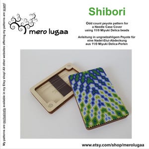Può includere: Un astuccio per aghi rettangolare con cornice in legno e una copertura in perline con un motivo geometrico Shibori blu, verde e bianco. L'astuccio è aperto e mostra un interno chiaro con diversi aghi in metallo riposti all'interno.