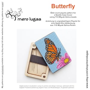 Könnte beinhalten: Eine Nadel-Etui-Abdeckung mit einem ungeradzahligen Peyote-Muster, das einen Monarchfalter auf hellblauem Grund mit einer rosa Blume zeigt. Das Etui ist aus hellem Holz und enthält mehrere Metallnadeln, die neben der Perlenabdeckung sichtbar sind.