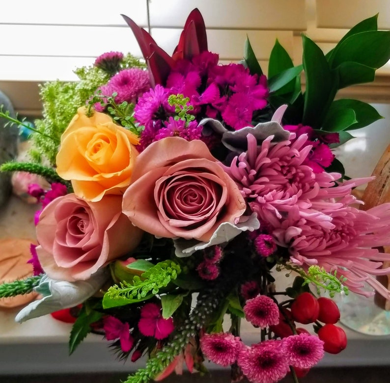 Puede incluir: Un ramo de flores rosas, naranjas y rojas con follaje verde. El ramo incluye rosas, claveles, crisantemos y otras flores.