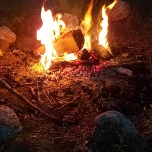Puede incluir: Una fogata ardiendo intensamente con llamas naranjas y amarillas. El fuego est&aacute; rodeado de rocas y tierra.