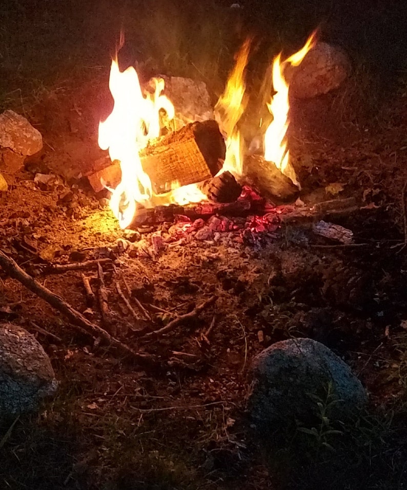Puede incluir: Una fogata ardiendo intensamente con llamas naranjas y amarillas. El fuego est&aacute; rodeado de rocas y tierra.