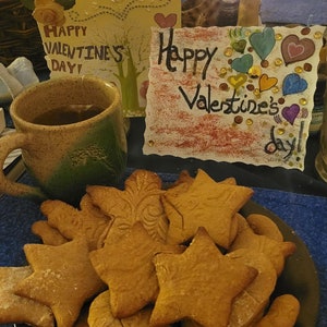 Puede incluir: Un plato de galletas de jengibre caseras con forma de estrellas y corazones. Las galletas est&aacute;n dispuestas en un plato marr&oacute;n oscuro. Hay dos tarjetas del D&iacute;a de San Valent&iacute;n en el fondo, una con el texto "&iexcl;Feliz D&iacute;a de San Valent&iacute;n!" y la otra con el texto "&iexcl;Feliz D&iacute;a de San Valent&iacute;n!"