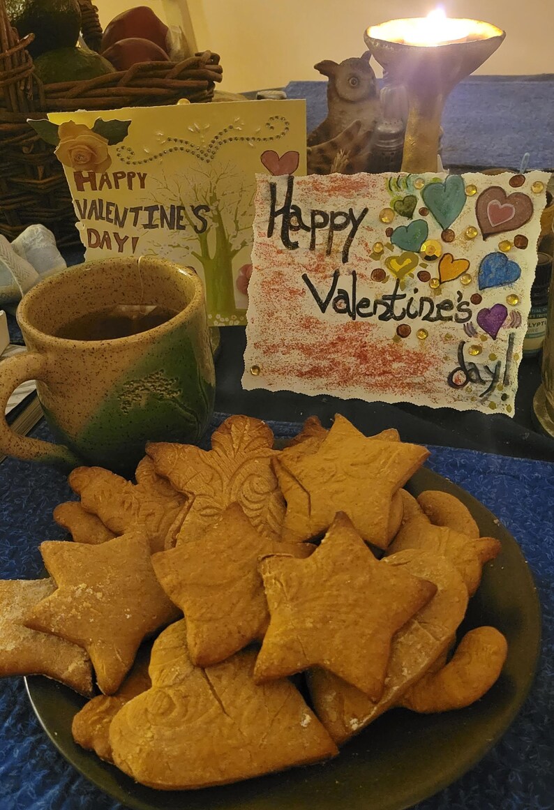 Puede incluir: Un plato de galletas de jengibre caseras con forma de estrellas y corazones. Las galletas est&aacute;n dispuestas en un plato marr&oacute;n oscuro. Hay dos tarjetas del D&iacute;a de San Valent&iacute;n en el fondo, una con el texto "&iexcl;Feliz D&iacute;a de San Valent&iacute;n!" y la otra con el texto "&iexcl;Feliz D&iacute;a de San Valent&iacute;n!"