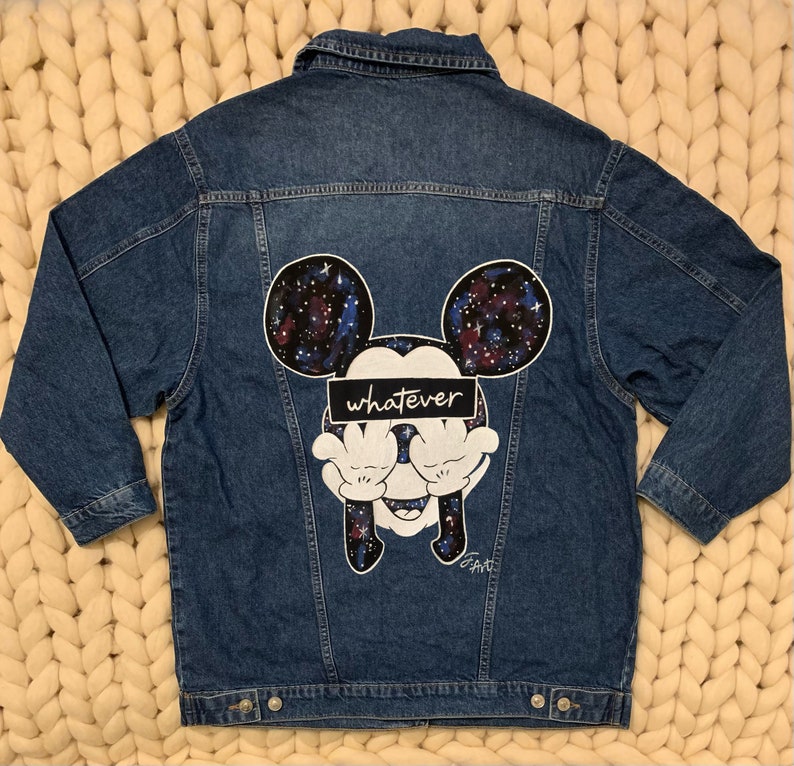 Op de afbeelding: Een blauwe denim jas met een Mickey Mouse-ontwerp met een galaxy-thema op de rug. Het ontwerp bevat het woord "whatever" over Mickey's ogen.