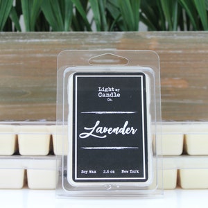 Puede incluir: Derretidos de cera con aroma a lavanda en un envase transparente de pl&aacute;stico. La etiqueta es negra con texto blanco que dice "Light by Candle Co." y "Lavender". Los derretidos de cera son de color crema claro. El fondo incluye una caja de madera y plantas verdes.