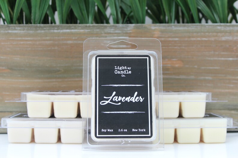 Puede incluir: Derretidos de cera con aroma a lavanda en un envase transparente de pl&aacute;stico. La etiqueta es negra con texto blanco que dice "Light by Candle Co." y "Lavender". Los derretidos de cera son de color crema claro. El fondo incluye una caja de madera y plantas verdes.