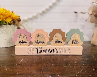May include: Four wooden turkey figurines with painted faces and names: Lydia, Shannon, Lucas, and Ben. The turkeys are sitting on a wooden block with the text "G-Ma Thompson's Gobblers".