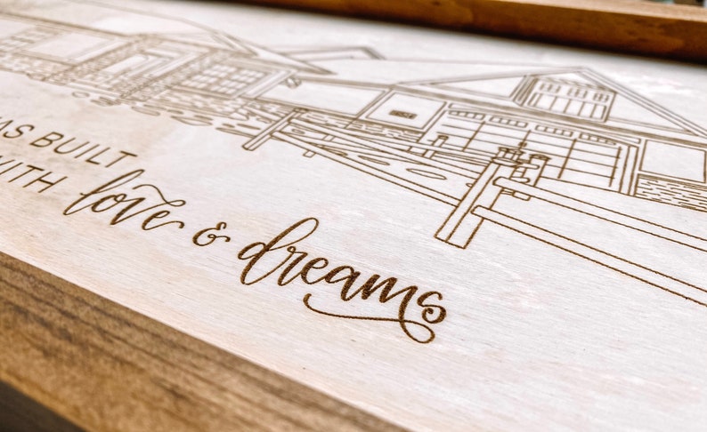 Puede incluir: Un letrero de madera con un dibujo de una casa y una cerca grabado con l&aacute;ser. El texto "Was built with love & dreams" tambi&eacute;n est&aacute; grabado en el letrero.