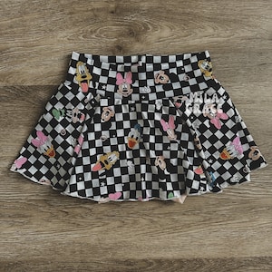 Puede incluir: Falda a cuadros negros y blancos con estampado de dibujos animados de personajes de Disney, incluyendo Mickey Mouse, Minnie Mouse, Donald Duck y Goofy.