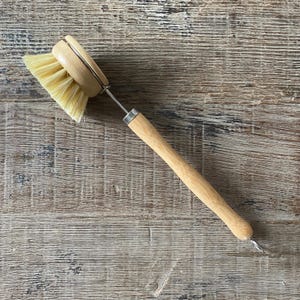 May include: A wooden dish brush with a long handle and a round brush head with natural bristles. The brush is designed for cleaning dishes and is made of sustainable materials.
