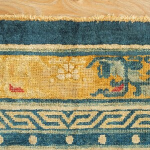 May include: Close-up of a blue and yellow rug with a geometric pattern. The rug has a fringe border and is made of woven fabric.
