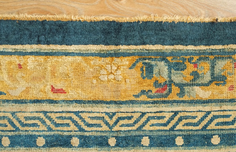 May include: Close-up of a blue and yellow rug with a geometric pattern. The rug has a fringe border and is made of woven fabric.