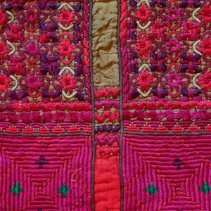 May include: Close-up of a colorful embroidered fabric with a beaded trim. The fabric is a mix of pink, red, and green, with intricate patterns and designs. The beads are white, orange, blue, and green.